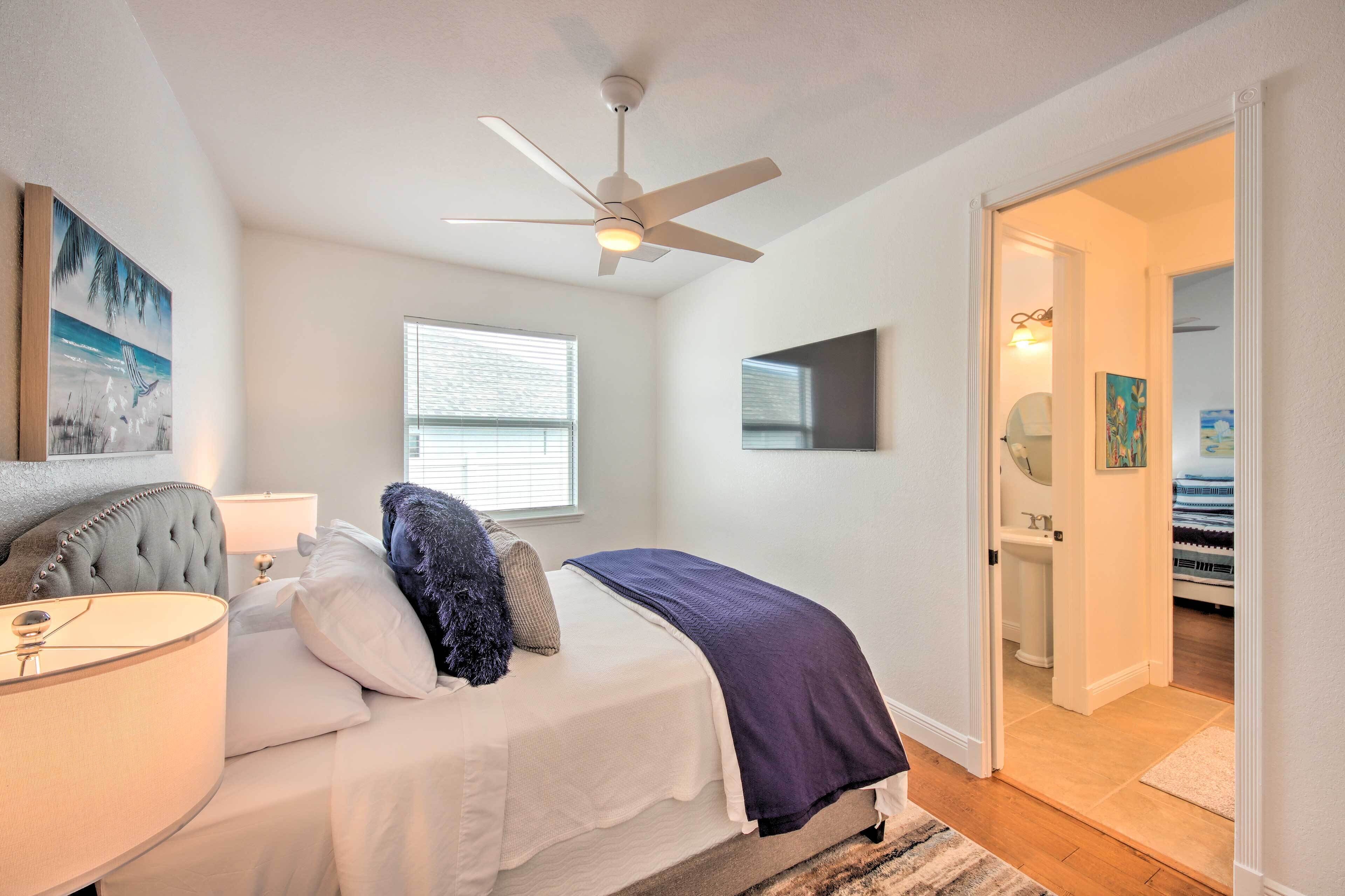 A bedroom with a bed, a ceiling fan, a window, and a door leading to a bathroom.
