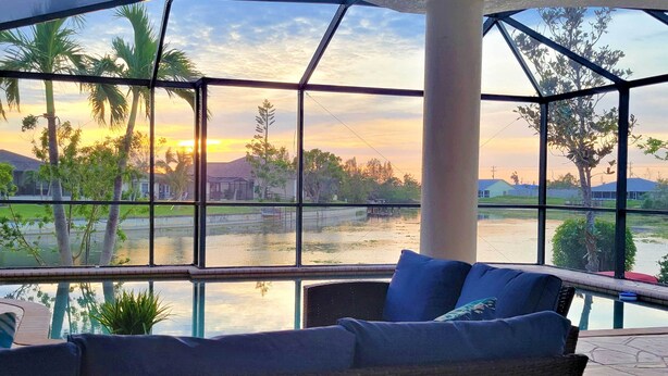 A room with a large glass window overlooking a body of water and palm trees. - On Canal: Luxe Cape Coral Oasis w/ Pool & Lanai! (Cape Coral)