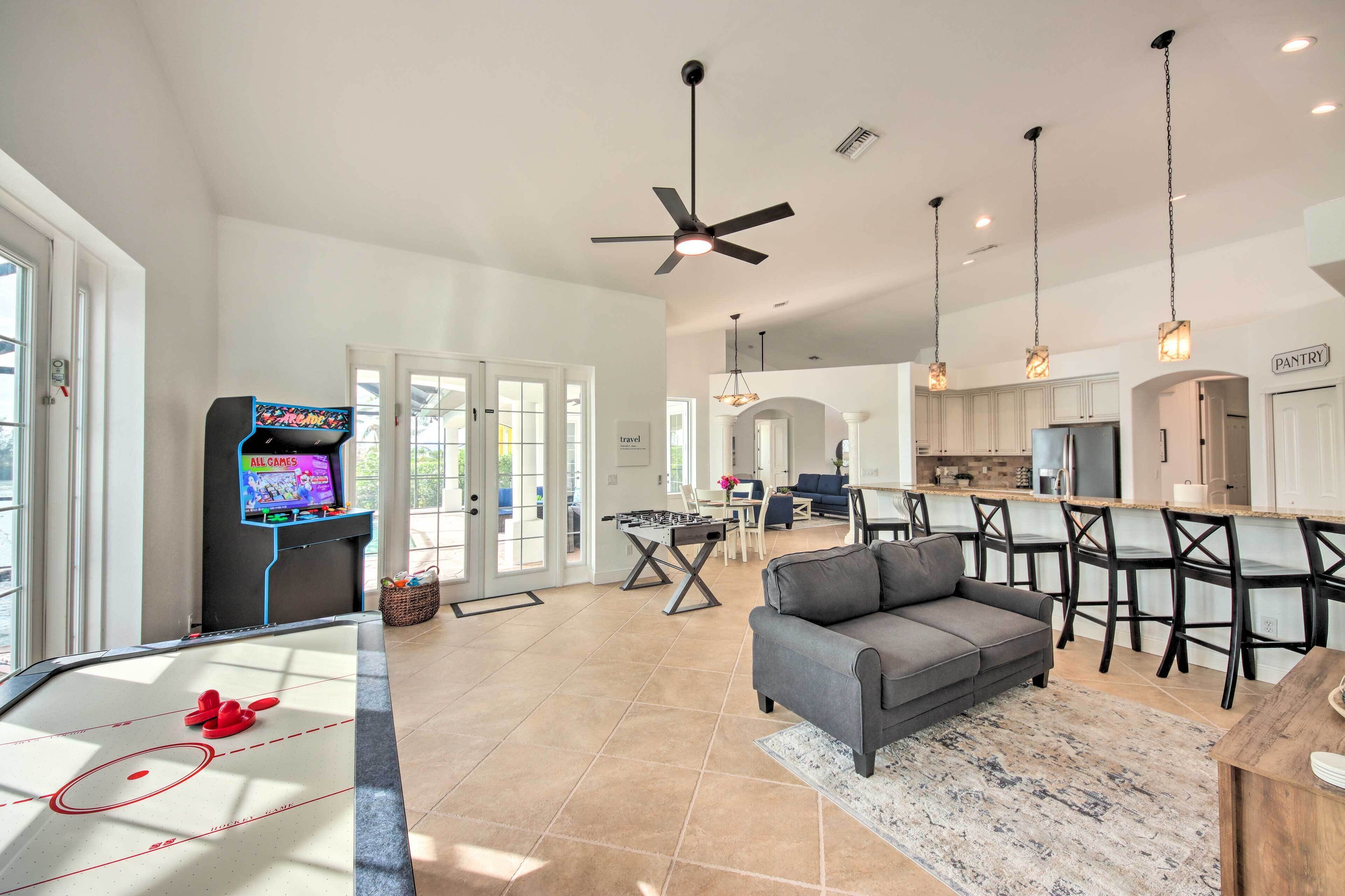 A spacious living area with a foosball table, a gray sofa, and a kitchen area with a dining table and chairs.