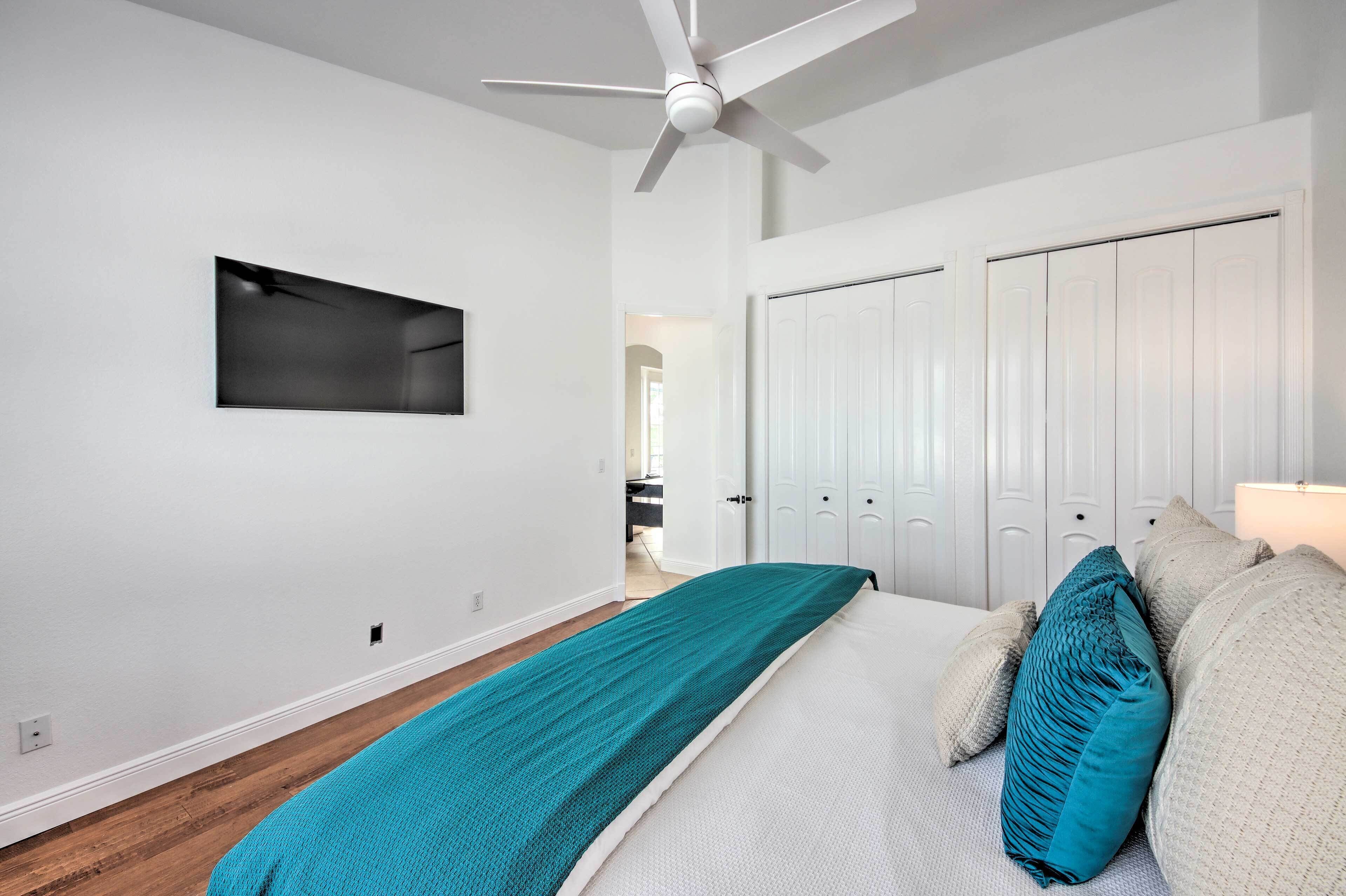 A bedroom with a bed, a ceiling fan, a wardrobe, and a door leading to another room.