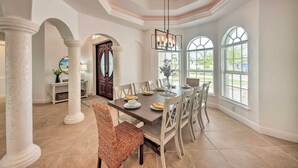 A dining area with a large table, chairs, and a chandelier. There are columns and large windows in the room. - On Canal: Luxe Cape Coral Oasis w/ Pool & Lanai! (Cape Coral)