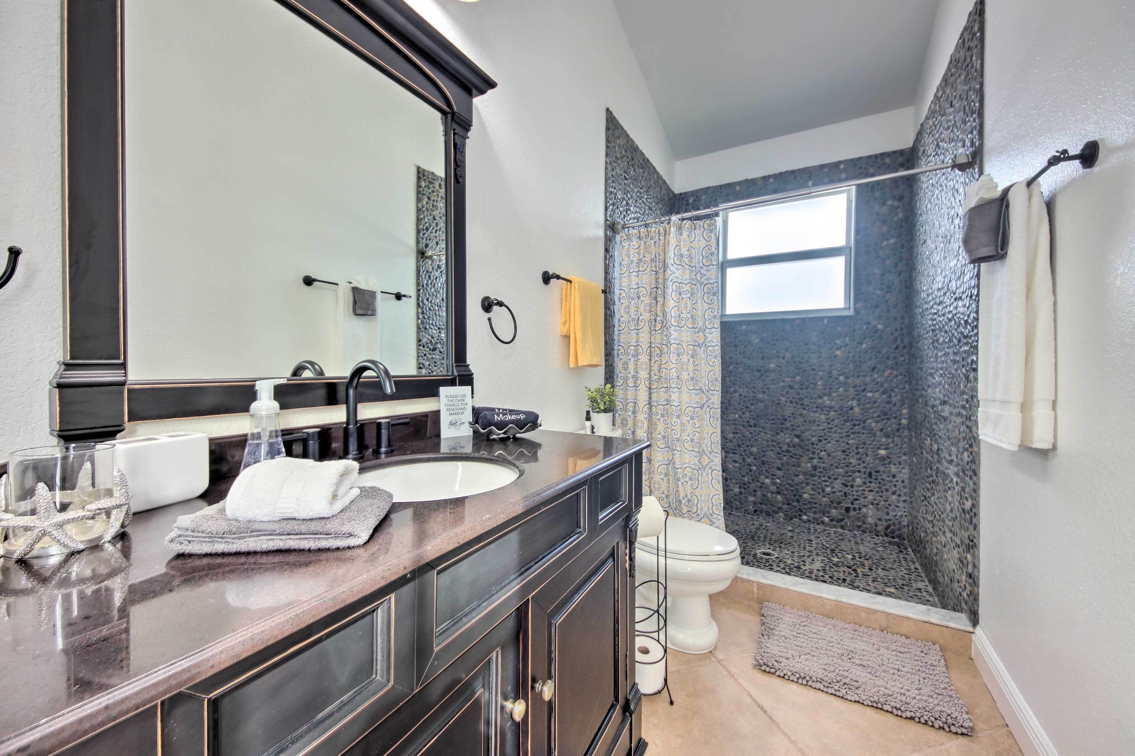 A bathroom with a large mirror, two sinks, a toilet, and a shower area with a patterned curtain.