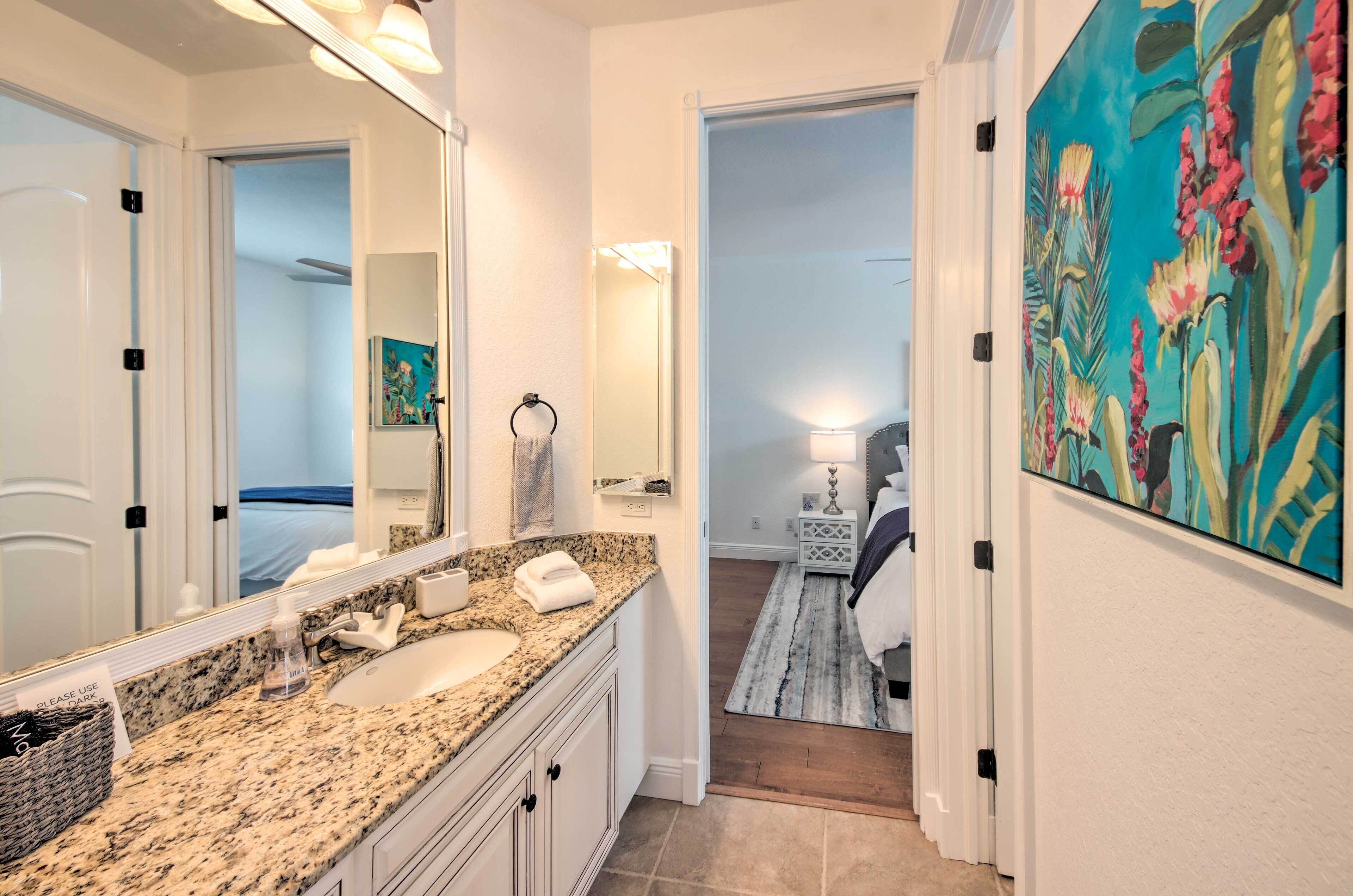 A bathroom with a granite countertop, a sink, a mirror, and a painting on the wall.