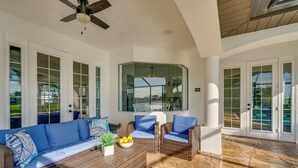 A covered patio area with wicker furniture, a glass door leading outside, and a stone floor. - On Canal: Luxe Cape Coral Oasis w/ Pool & Lanai! (Cape Coral)