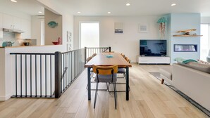 A modern kitchen with white cabinets, a wooden dining table, and a black railing. - Scenic Depoe Bay Townhome w/ Deck < 1 Mi to Parks! (Depoe Bay)