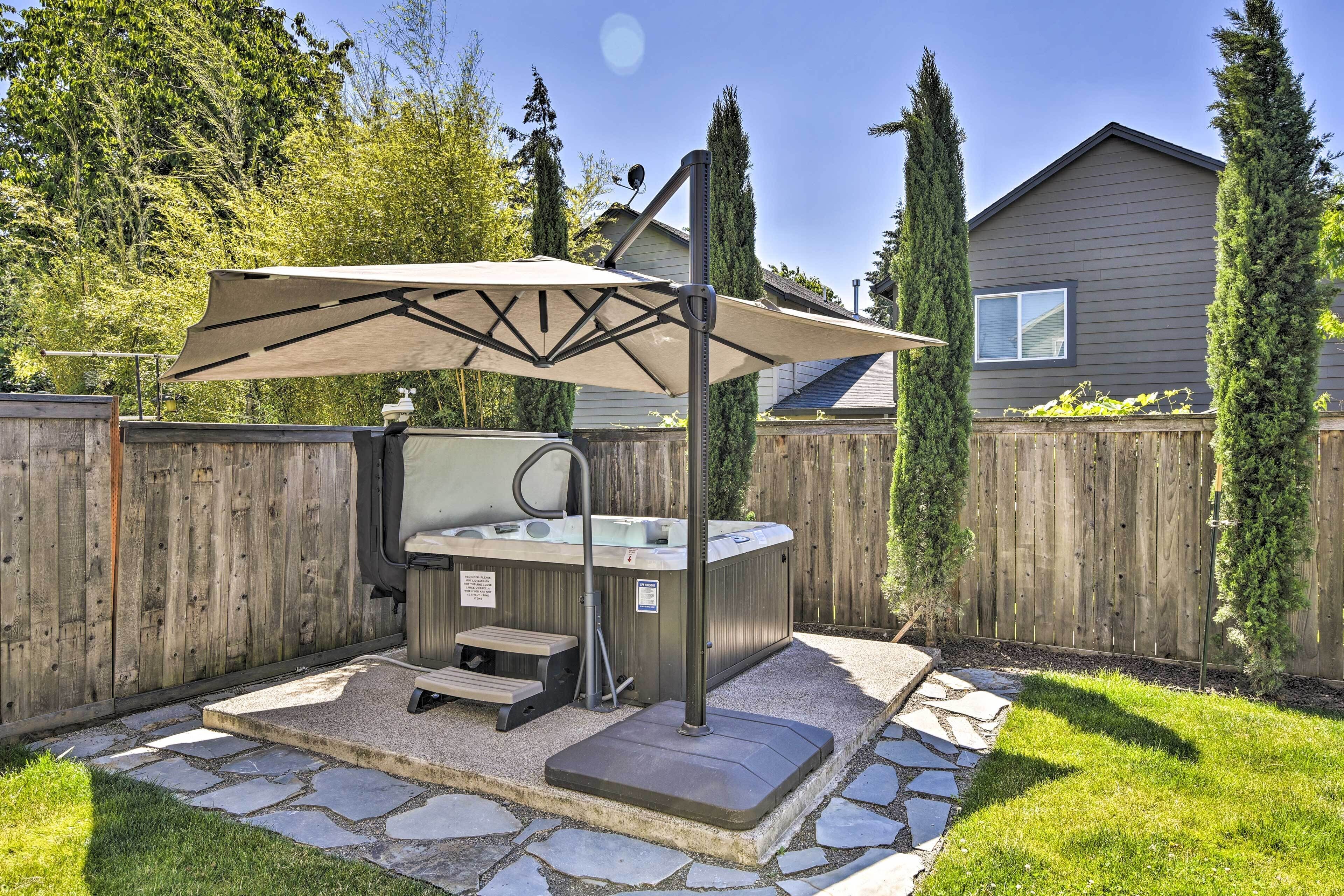 A hot tub with a canopy, stone steps, and a wooden fence in a backyard.