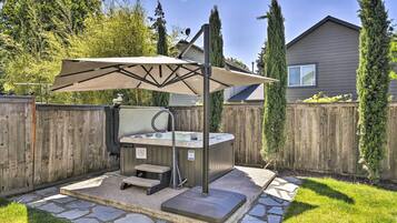 A hot tub with a canopy, stone steps, and a wooden fence in a backyard.