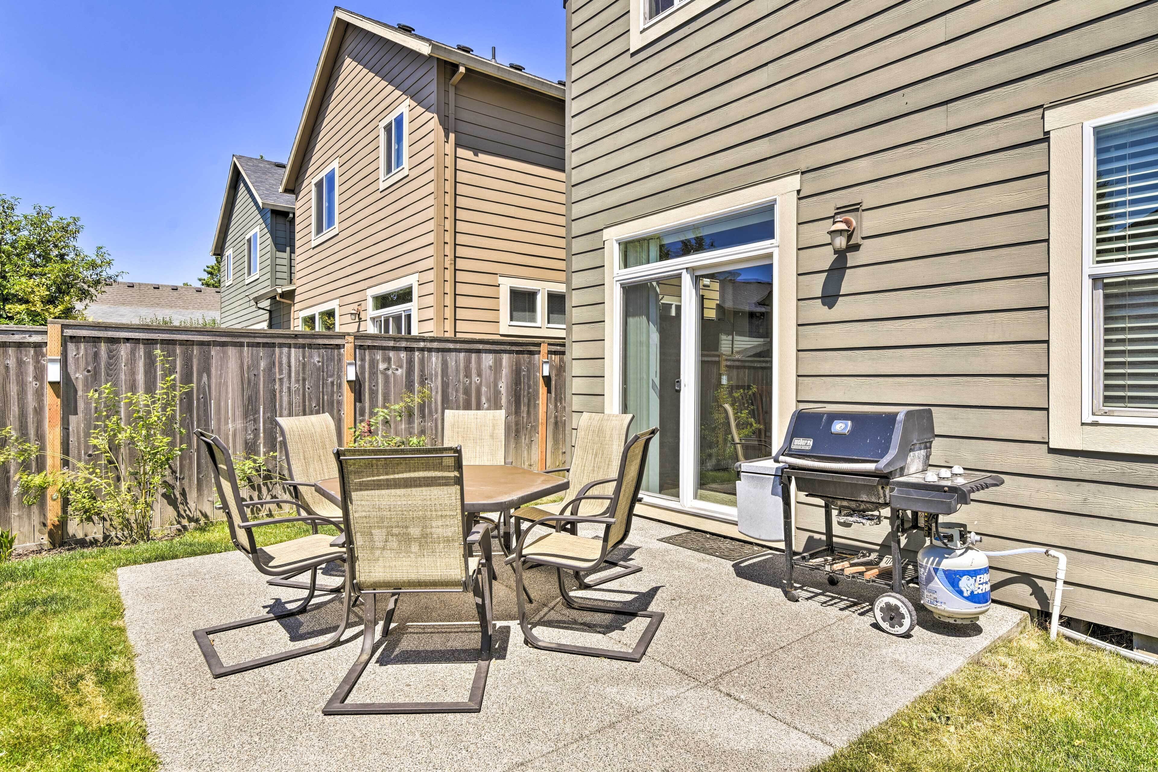A patio with a table and chairs, a grill, and a propane tank.