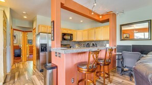 A compact kitchen with a central island, wooden bar stools, and a dining area with a gray chair and a black couch. - Cozy Condo w/ Views, 3 Mi to Winter Park Resort! (Winter Park)
