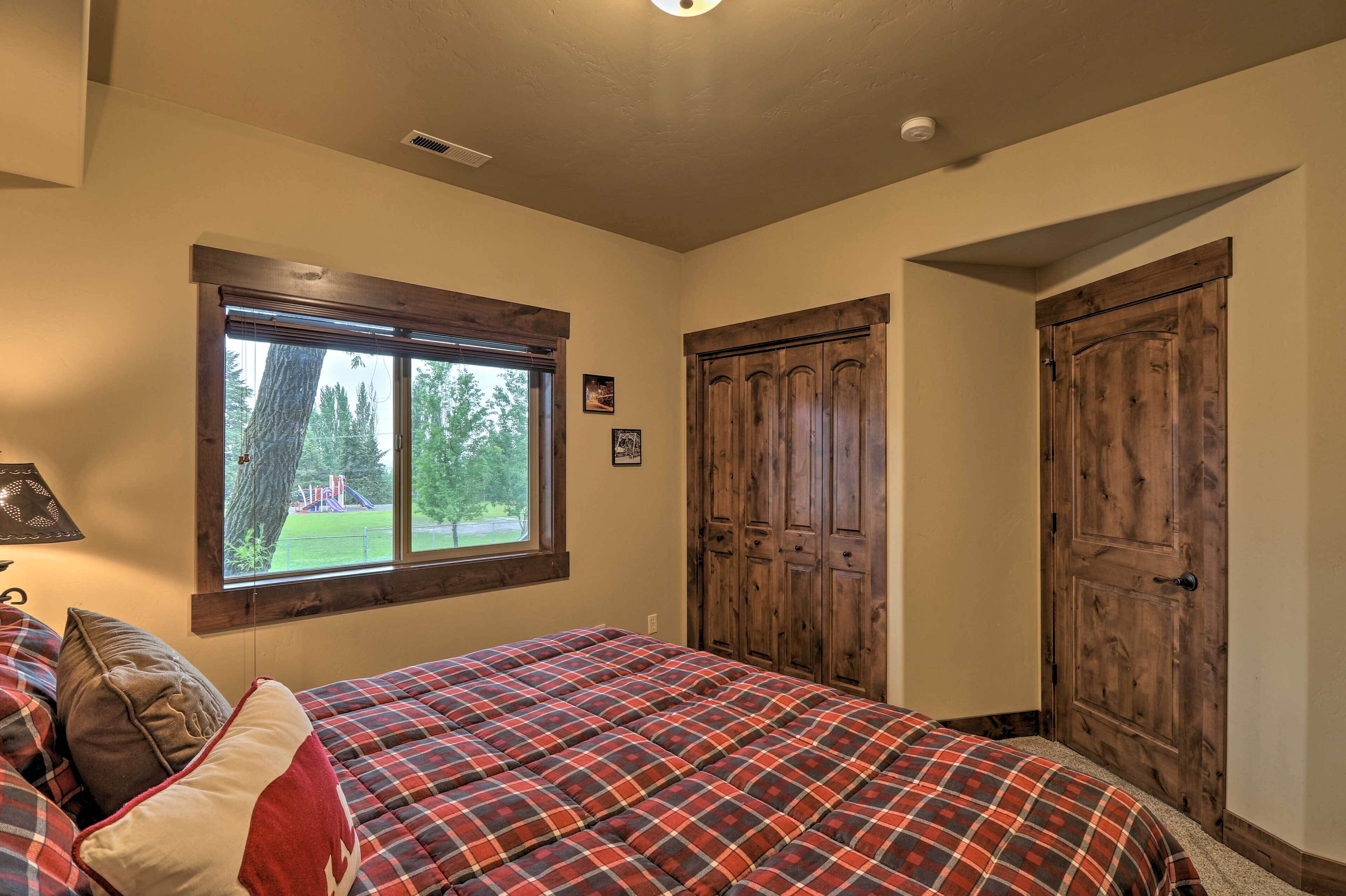 A bedroom with a plaid bedspread, a window with a view of trees, and wooden doors.
