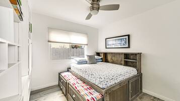 Een slaapkamer met een houten bed, een plafondventilator, een raam met zonwering en een boekenplank.
