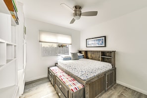 A bedroom with a wooden bed, a ceiling fan, a window with blinds, and a bookshelf.