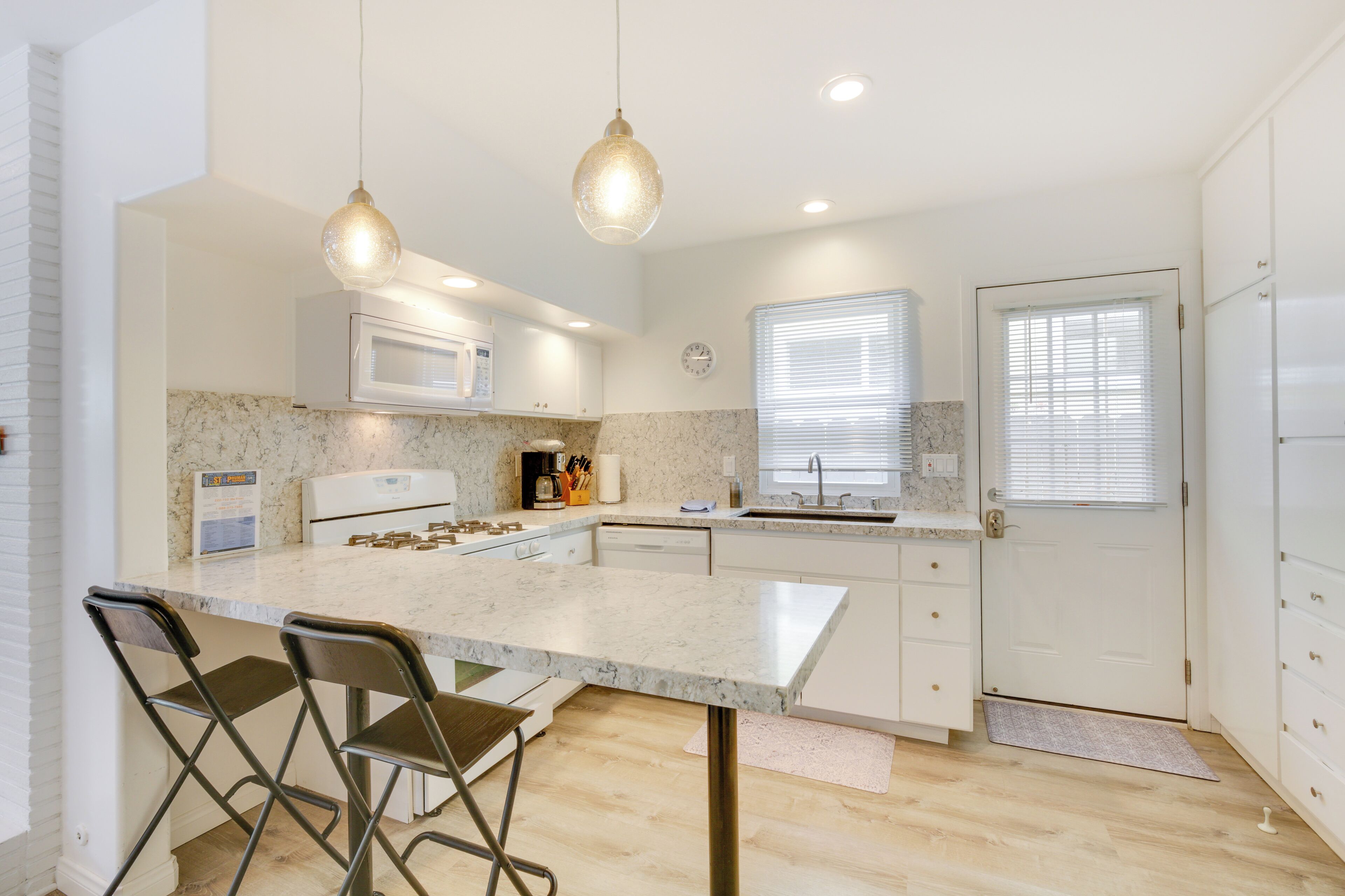 A modern kitchen with a marble countertop, two bar stools, a microwave, and a sink.