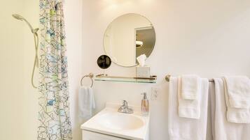 A bathroom with a shower, a sink, a mirror, and towels.