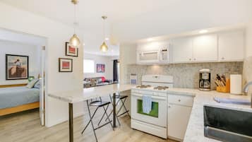 A modern kitchen with white cabinets, a built-in microwave, and a gas stove. There is a bar area with stools and a painting on the wall.