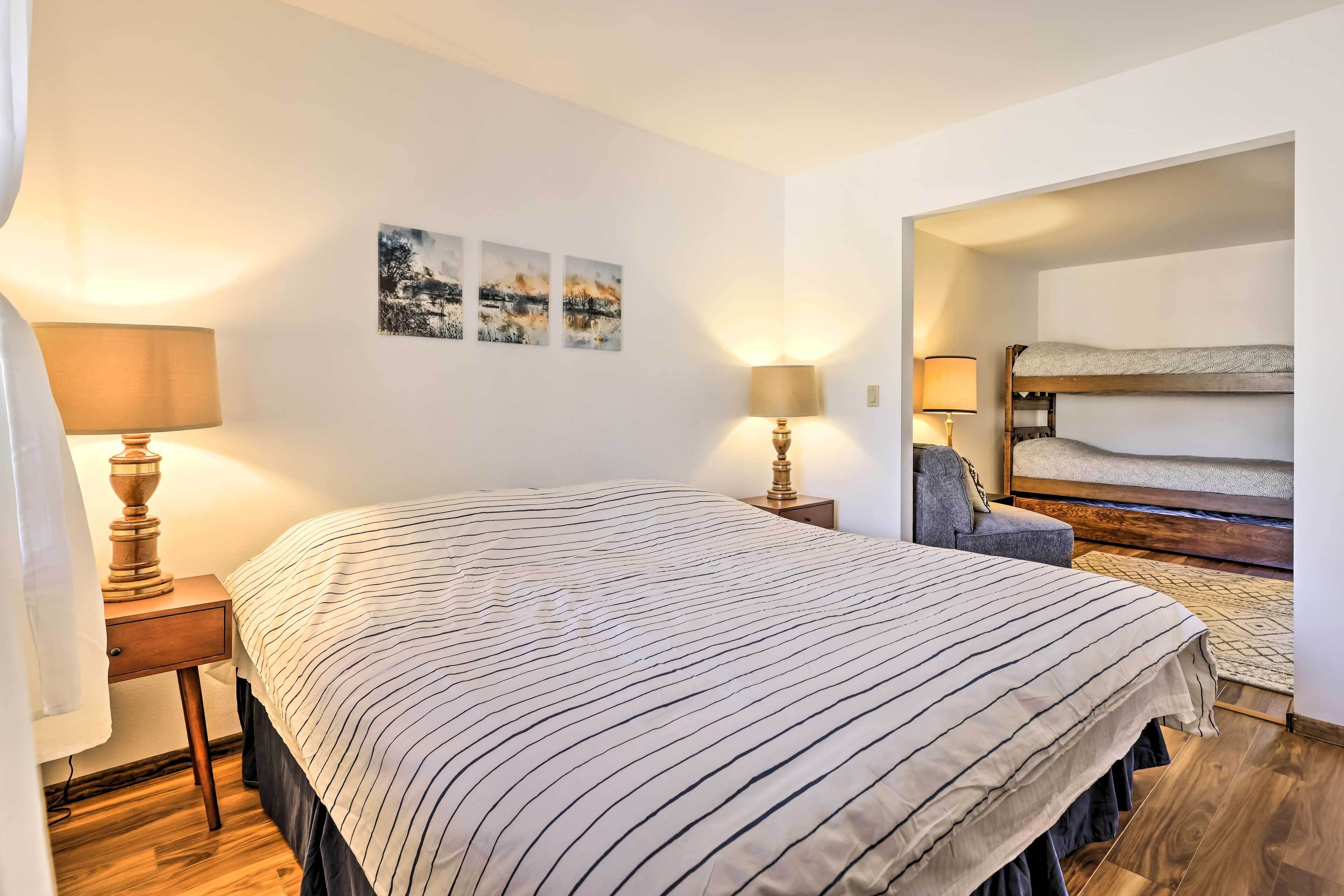 A bedroom with a large bed, two bedside tables with lamps, a bunk bed, and three wall-mounted pictures.