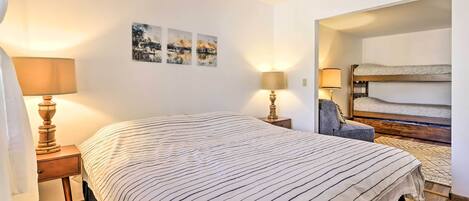 A bedroom with a large bed, two bedside tables with lamps, a bunk bed, and three wall-mounted pictures.