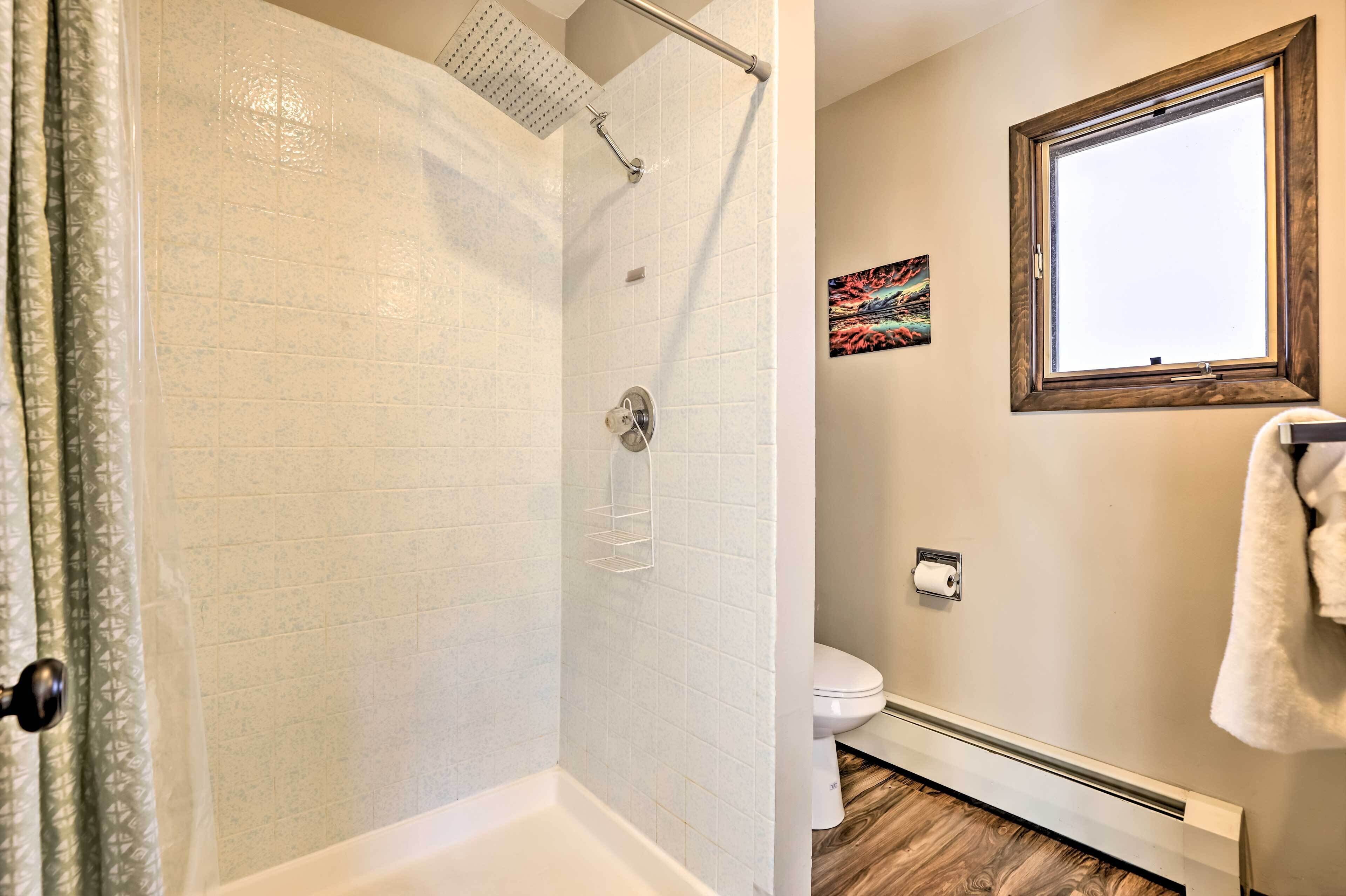 A bathroom with a shower, toilet, and a window.