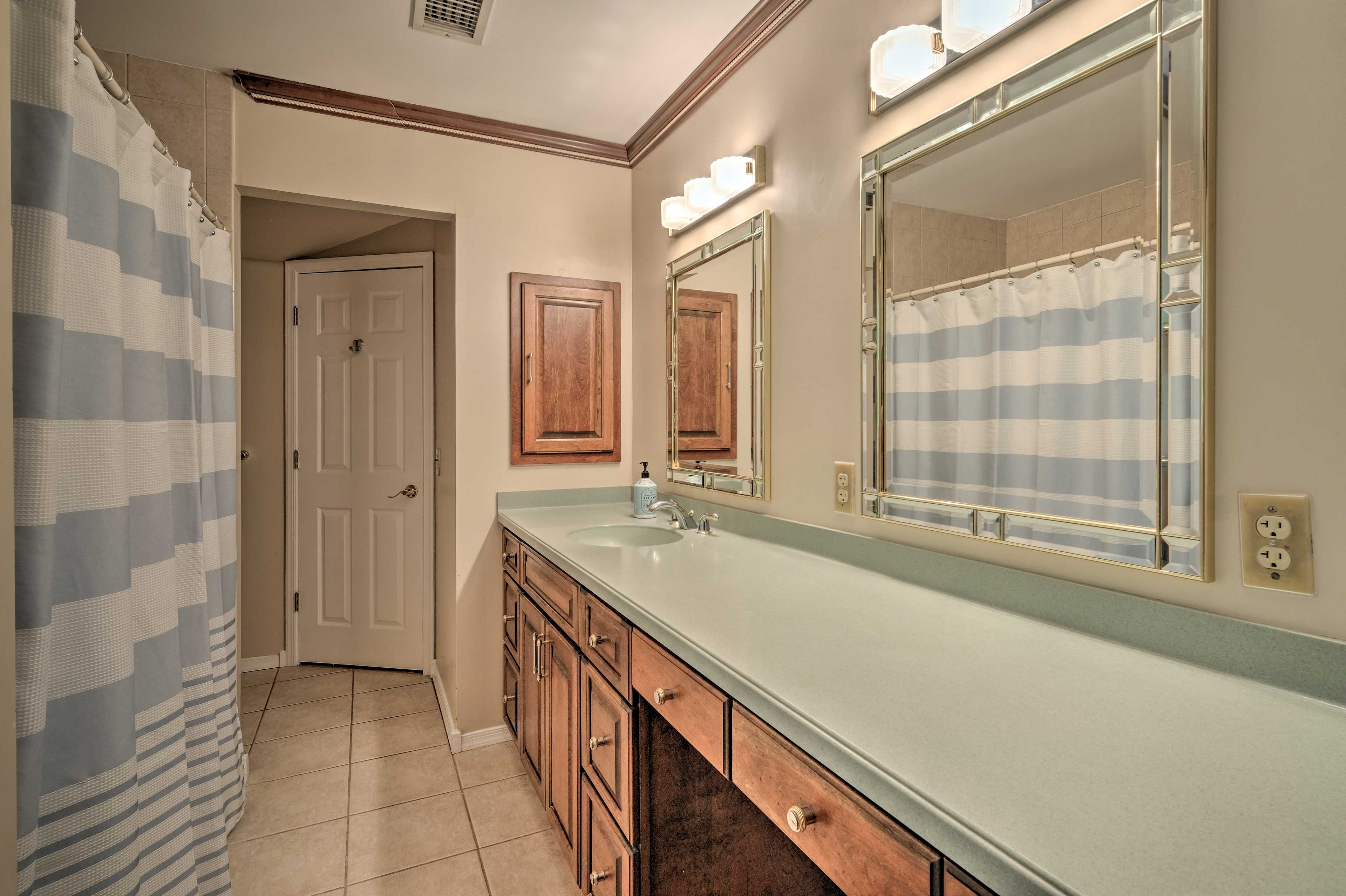 A bathroom with a large mirror, two sinks, wooden cabinets, and a striped shower curtain.