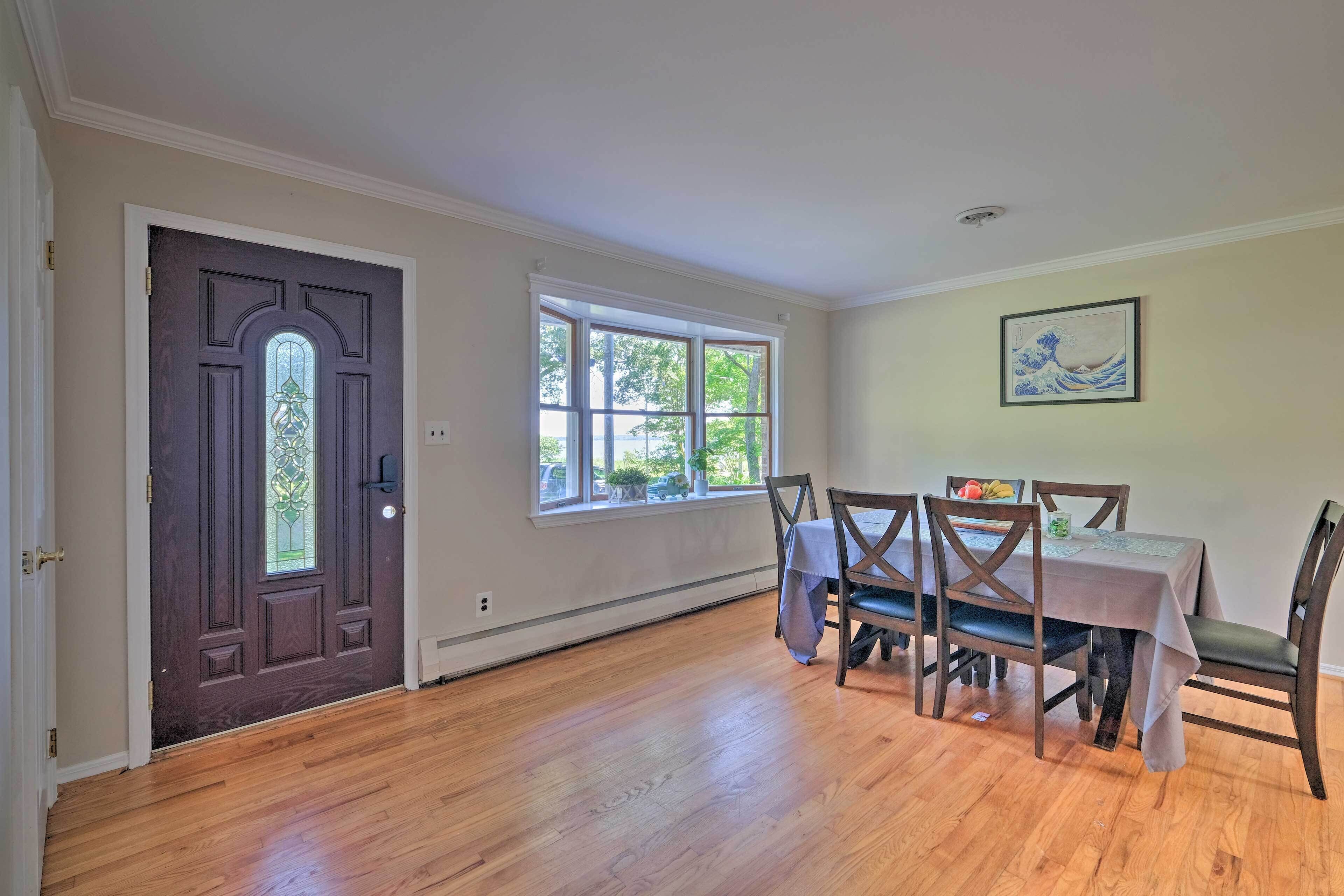 A dining room with a wooden table and chairs, a large window, and a door with a decorative glass panel.