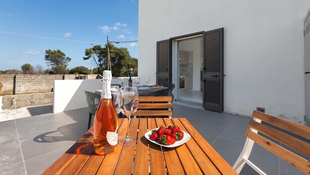 Eine Terrasse im Freien mit einem Holztisch, Erdbeeren auf einem Teller, einer Weinflasche und einer Sitzbank.