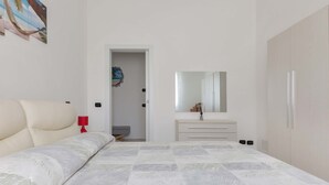 Ein Schlafzimmer mit Bett, Nachttisch, Kommode, Spiegel und einer Tür zu einem anderen Raum.