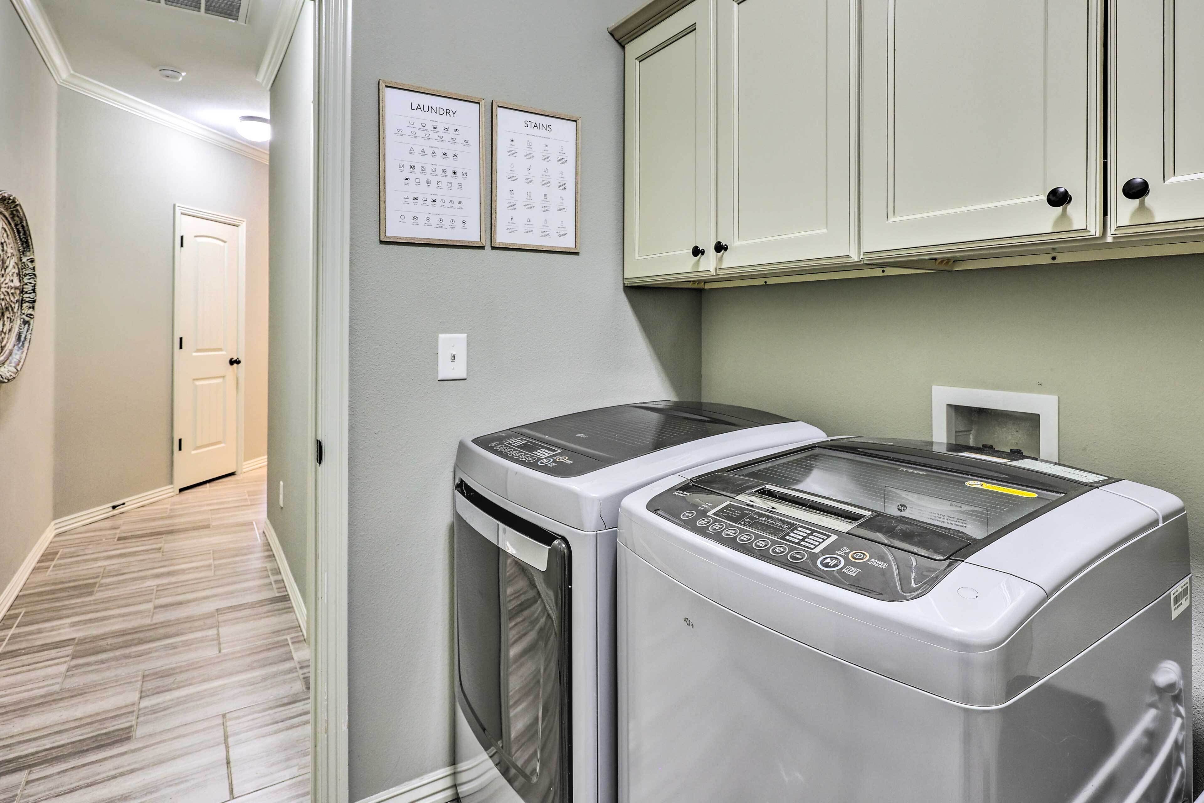 A laundry room with two front-loading washing machines, a wall-mounted dryer, and two framed laundry charts on the wall.