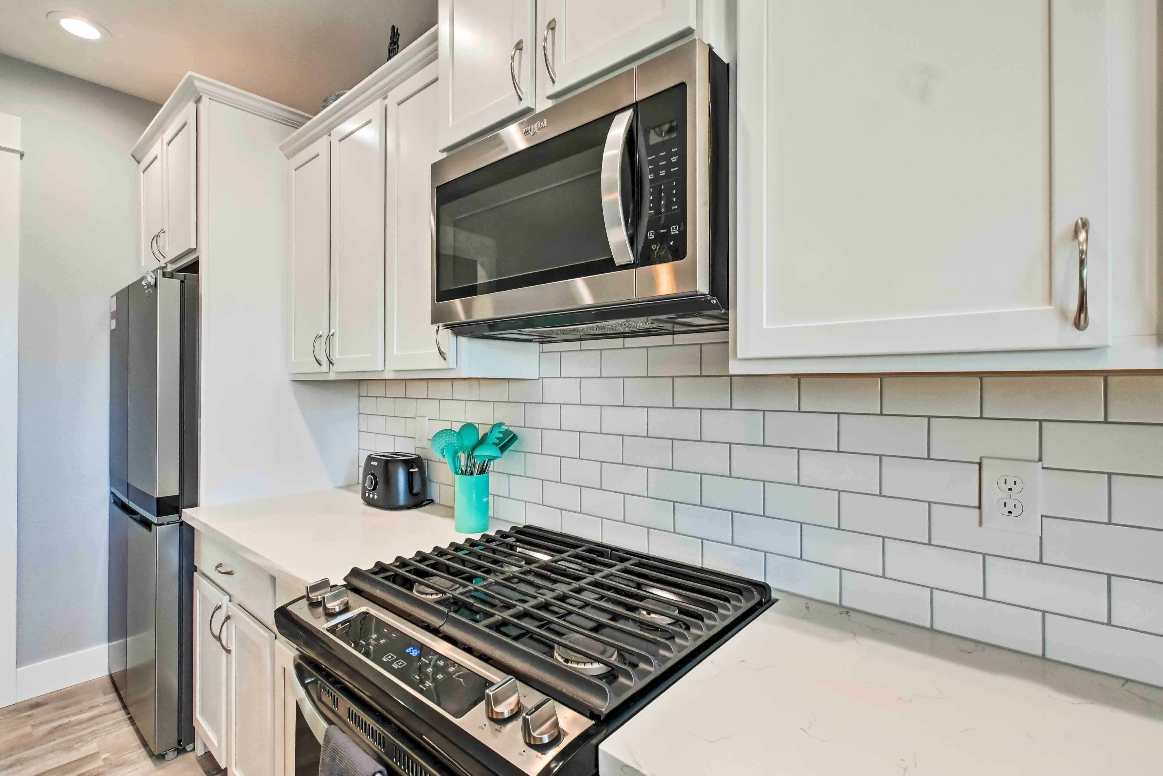A modern kitchen with white cabinets, a stainless steel microwave, a gas stove, and a built-in oven.