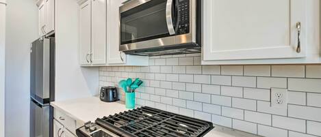 A modern kitchen with white cabinets, a stainless steel microwave, a gas stove, and a built-in oven.