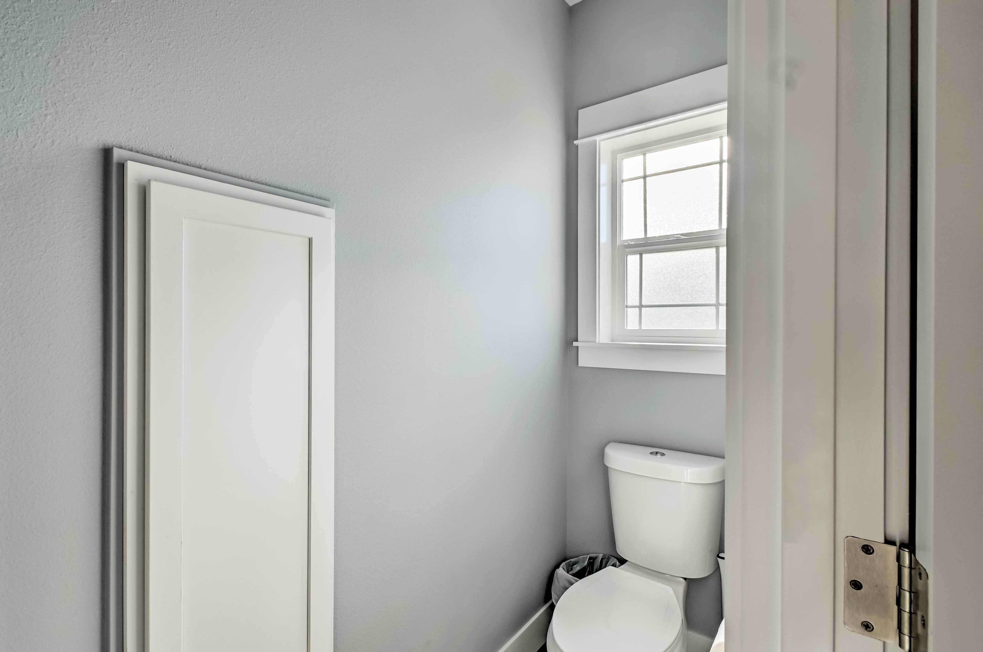 Un baño con un inodoro blanco, una ventana sobre el inodoro y una puerta a la izquierda.