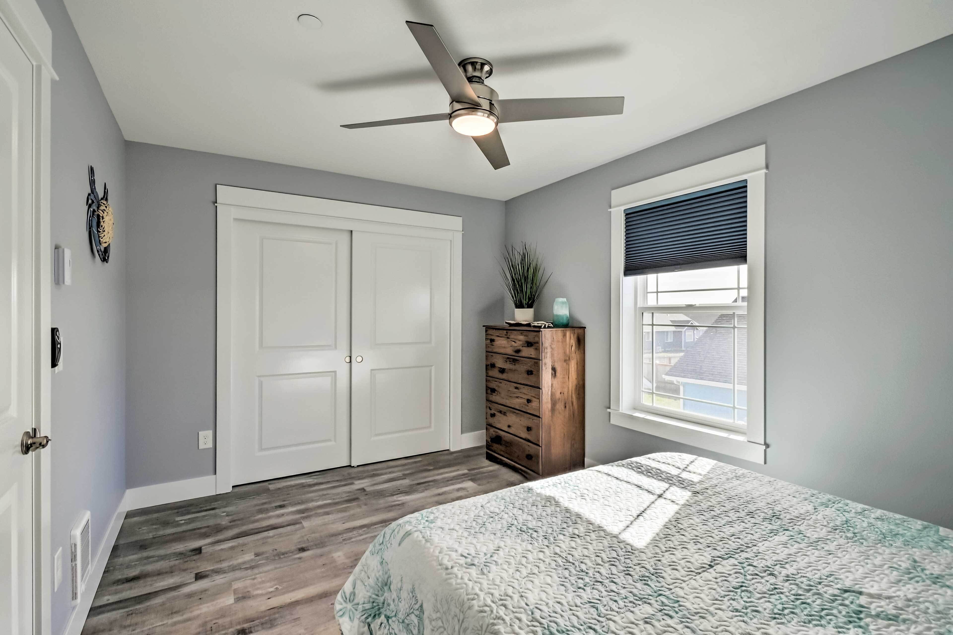 A bedroom with a bed, a ceiling fan, a dresser, a window with blinds, and a door.