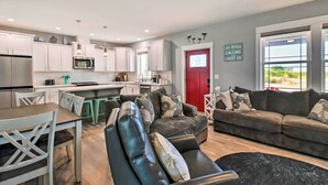 A modern kitchen with white cabinets, a red door, and a dining area with a table and chairs. - Ocean Shores Getaway w/ Fireplace & Hot Tub! (Ocean Shores)