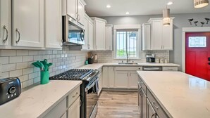 A modern kitchen with white cabinets, a gas stove, and a red door. - Ocean Shores Getaway w/ Fireplace & Hot Tub! (Ocean Shores)