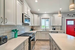 A modern kitchen with white cabinets, a gas stove, and a red door. - Ocean Shores Getaway w/ Fireplace & Hot Tub! (Ocean Shores)