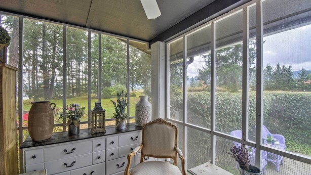 Une véranda dotée d’une grande fenêtre, d’un meuble en bois, d’une chaise et d’une petite table sur laquelle est posé un vase.