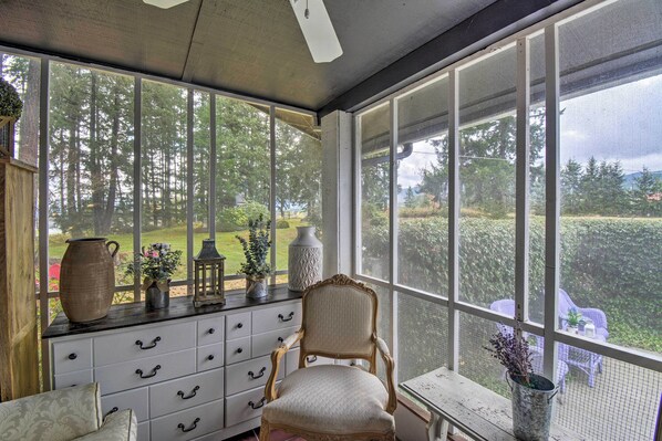 A conservatory with a large window, a wooden cabinet, a chair, and a small table with a vase. - Spacious Home w/ Yard, 20 Miles to Olympic NP (Sequim)