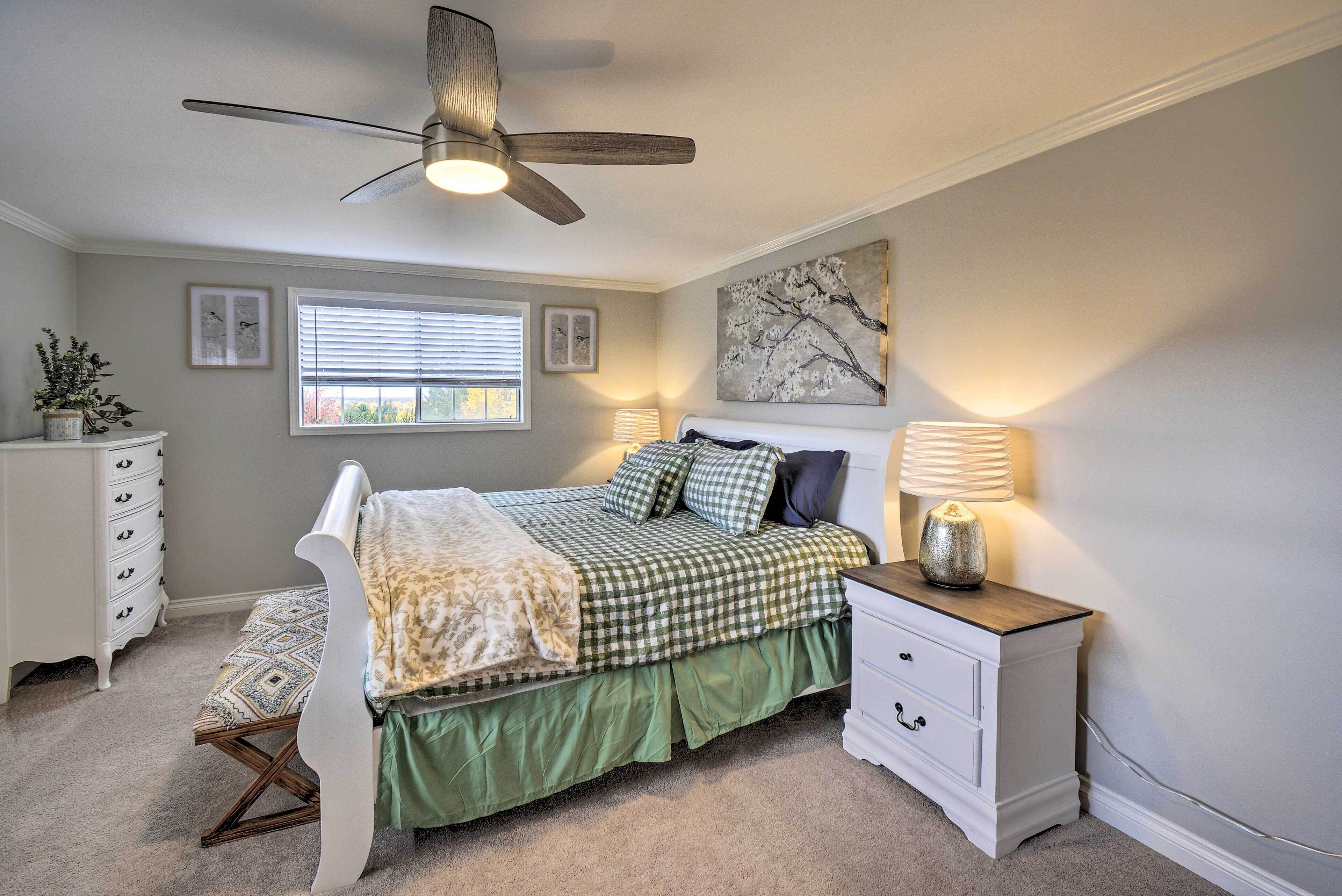 A bedroom with a bed, a nightstand, a dresser, a ceiling fan, and a window with blinds.