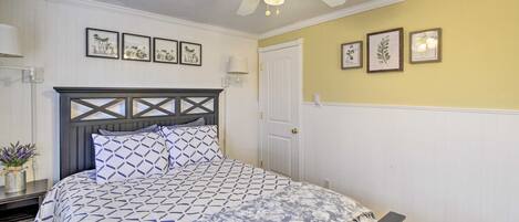A bedroom with a bed, a ceiling fan, and wall-mounted artwork.