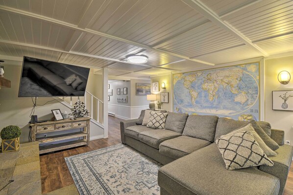 Una sala de estar con un sofá grande, un televisor, un mapa del mundo en la pared y una escalera que conduce a otra habitación.