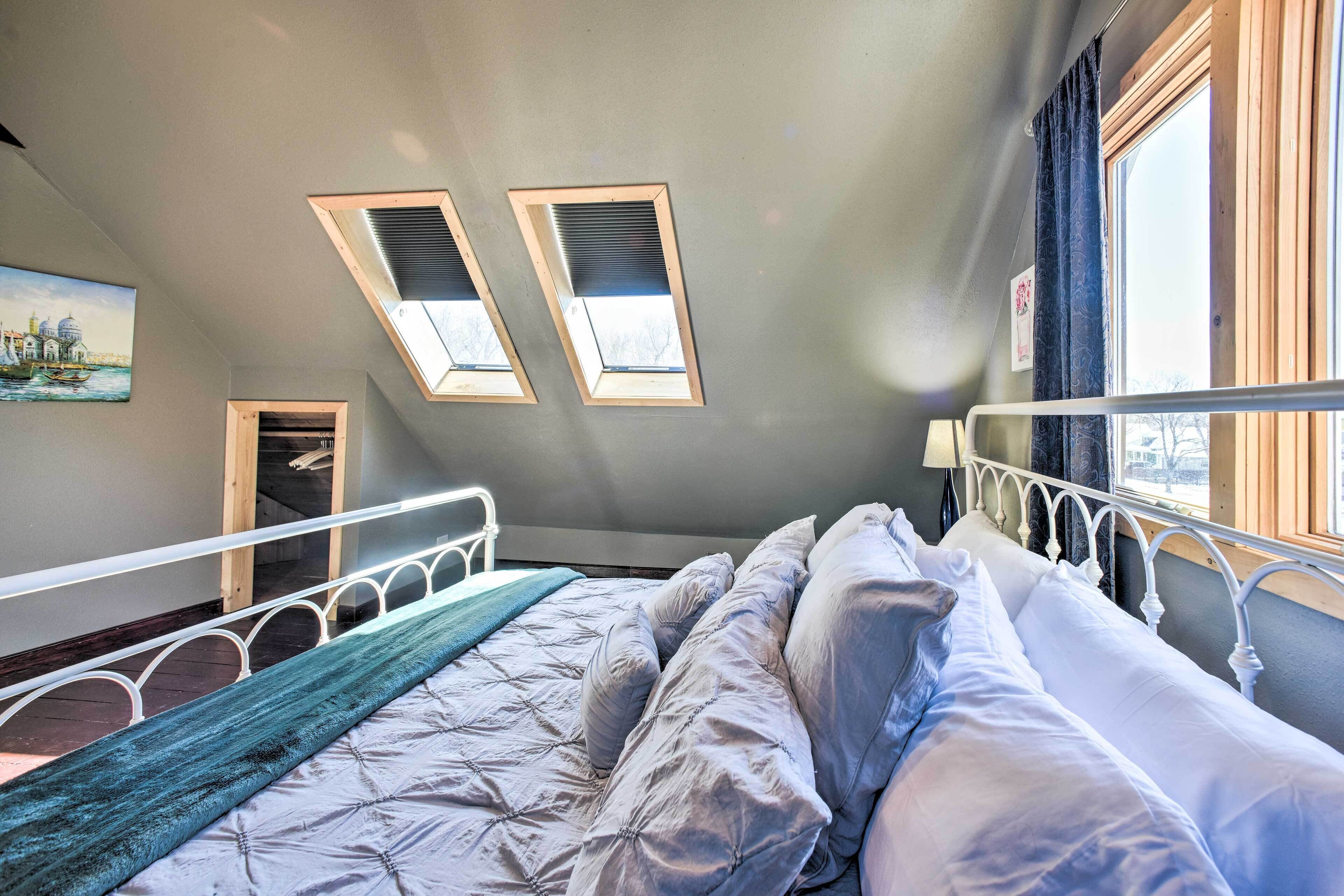 A bedroom with a bed, skylights, a window, and a painting on the wall.