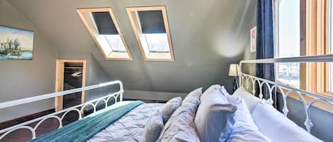 A bedroom with a bed, skylights, a window, and a painting on the wall.