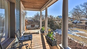 A covered porch with a wooden deck, two chairs, a bench, and planters with yellow flowers. - Historic Old Colorado City Home w/ Backyard! (Colorado Springs)