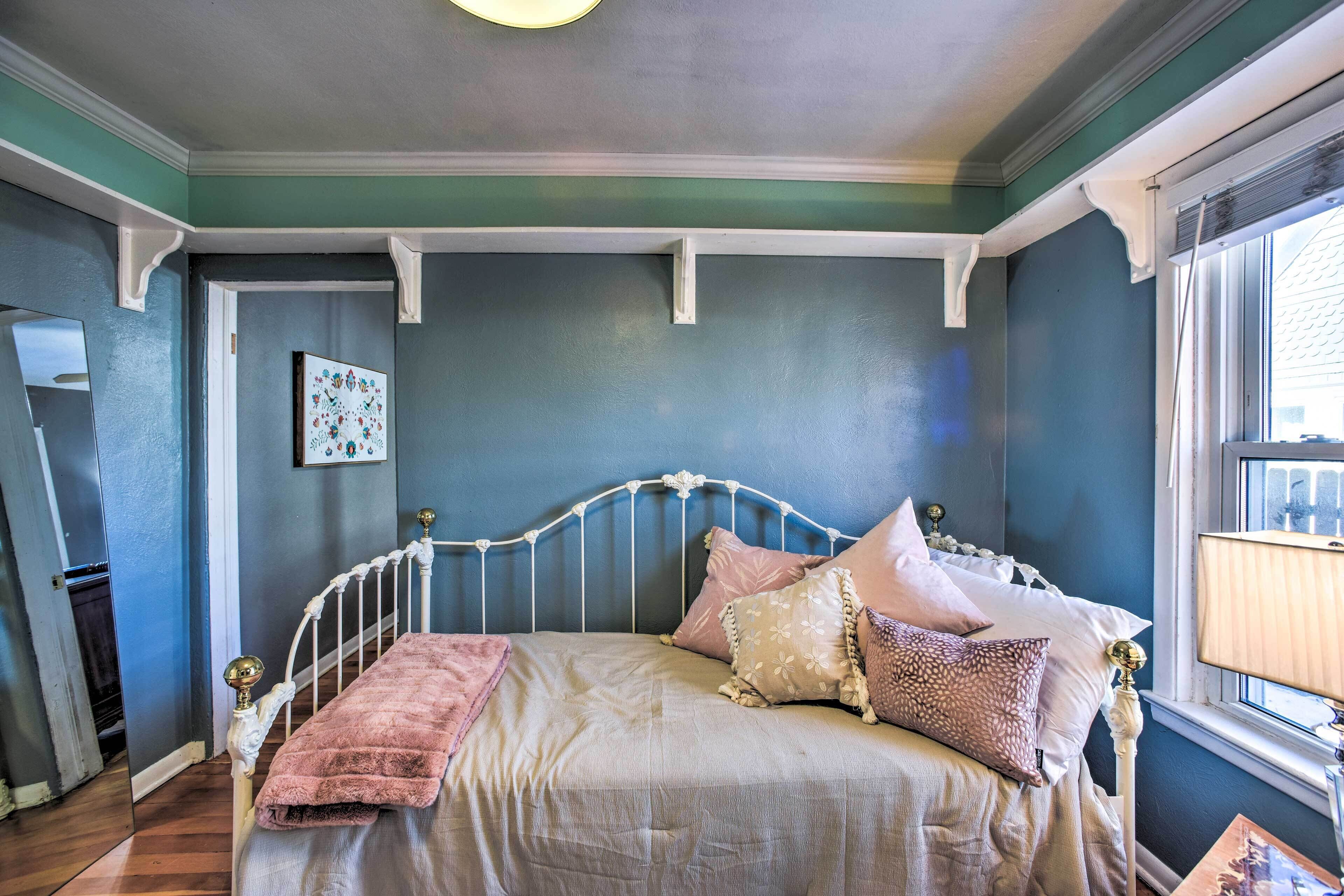 Une chambre avec un lit en métal blanc, un mur bleu et une fenêtre donnant sur l’extérieur.
