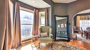 A room with a patterned armchair, a large mirror, and a view of a cityscape through a window with curtains. - Historic Old Colorado City Home w/ Backyard! (Colorado Springs)