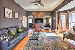 A modern living room with a grey sofa, a coffee table, and a world map on the wall. - Historic Old Colorado City Home w/ Backyard! (Colorado Springs)