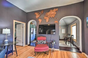 A living room with a red armchair, a glass table, a flat-screen TV mounted on the wall, and a world map decoration. - Historic Old Colorado City Home w/ Backyard! (Colorado Springs)