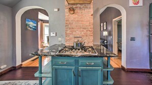 A kitchen with a central island, blue cabinets, and a brick wall. - Historic Old Colorado City Home w/ Backyard! (Colorado Springs)