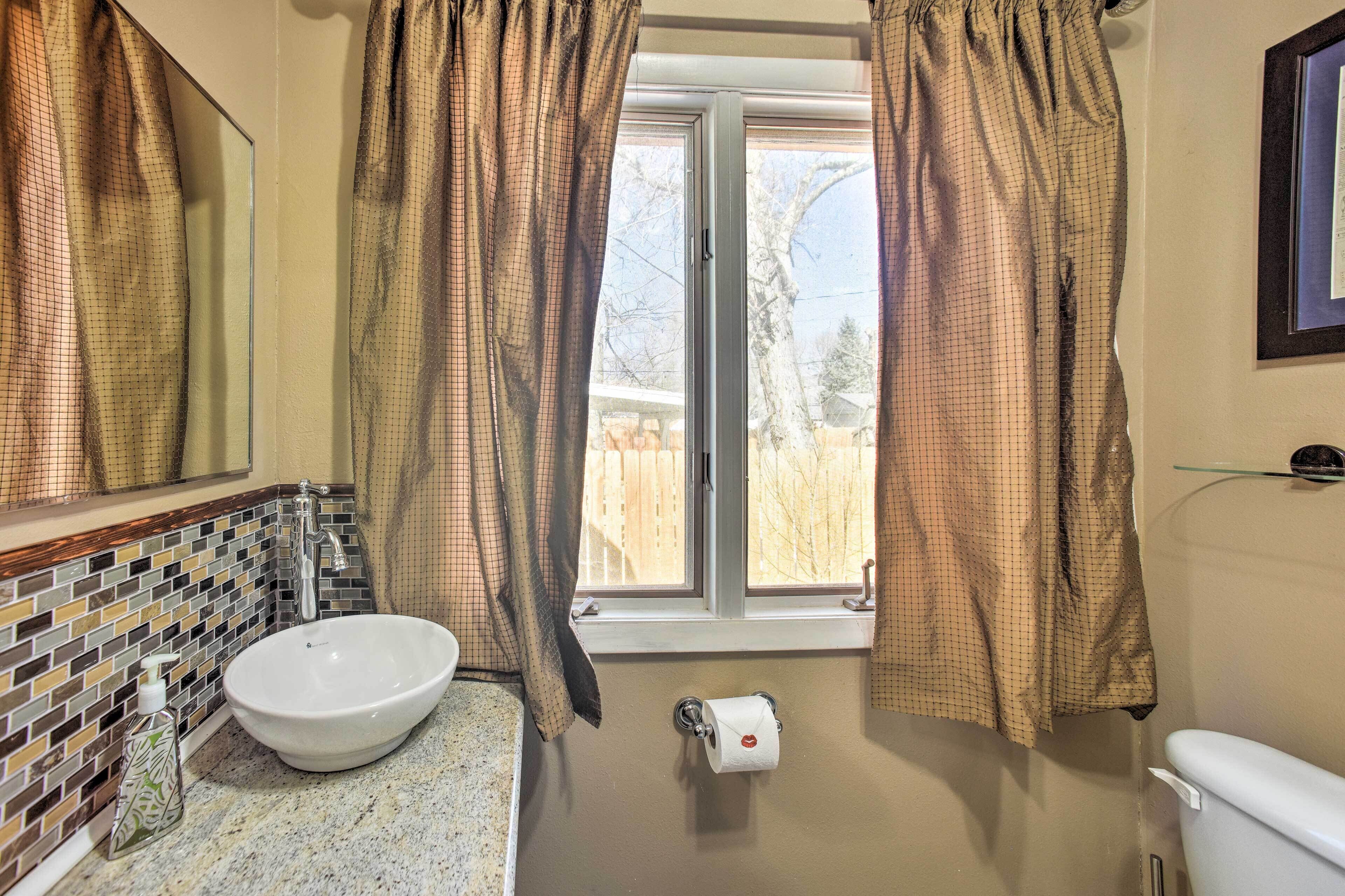 Un baño con un lavamanos blanco, un espejo, un inodoro y una ventana con cortinas.