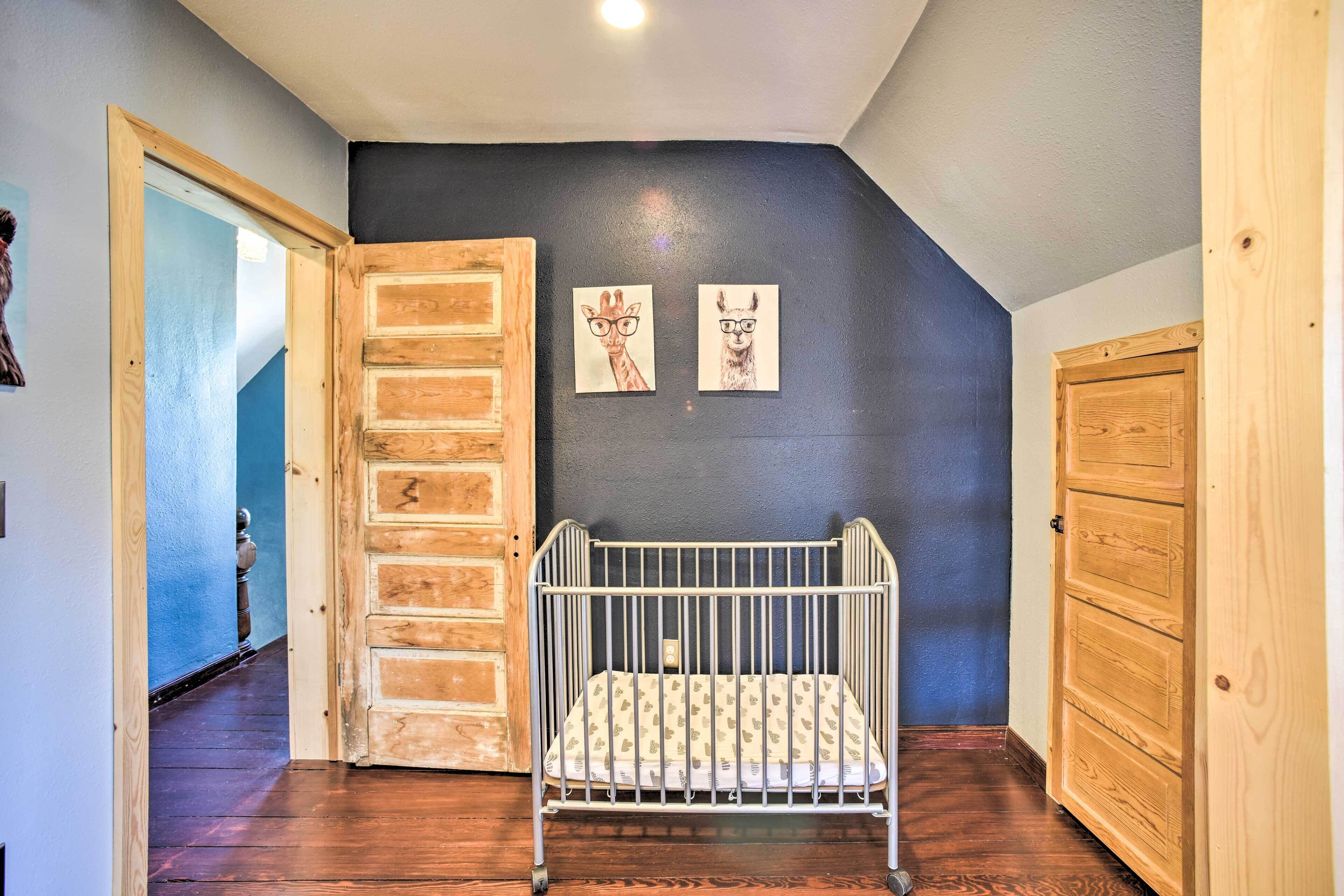 A room with a crib, wooden cabinets, and a dark wall with two framed drawings.