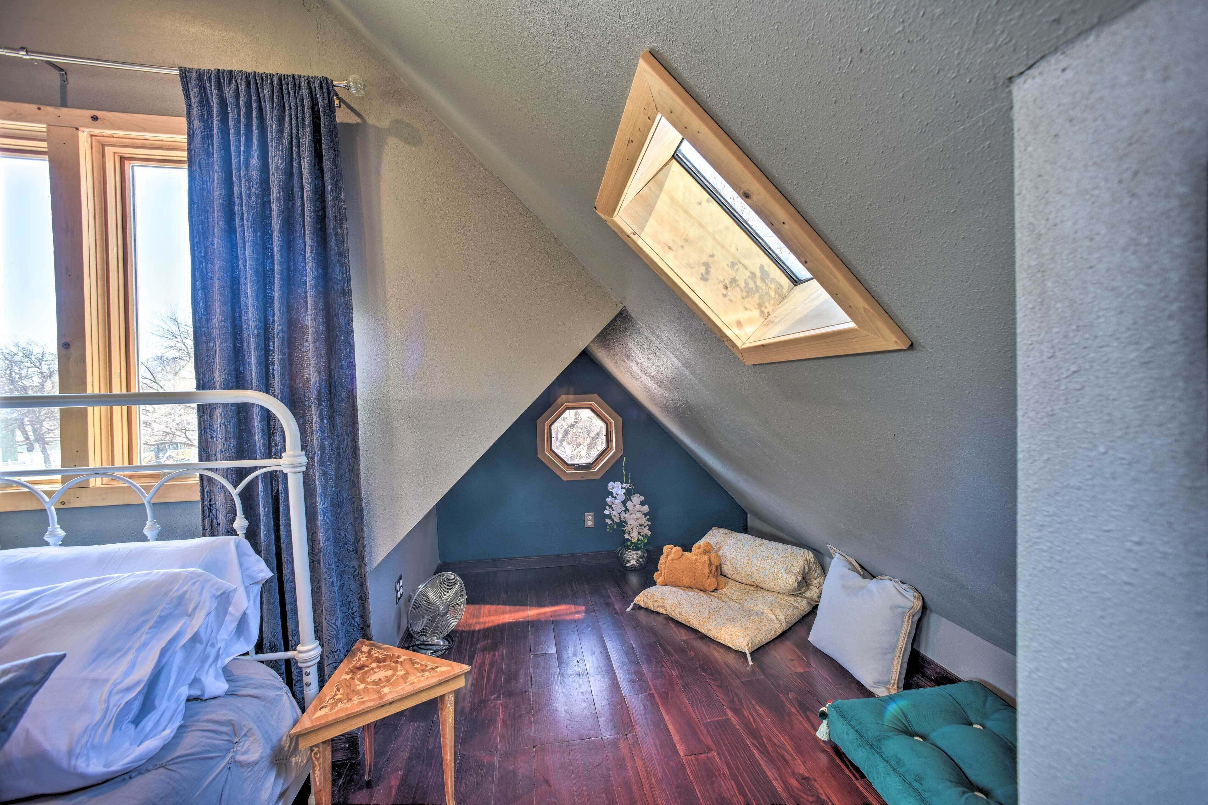 Et soveværelse med seng, et lille bord, en ventilator, en sofa og et vindue med gardiner.